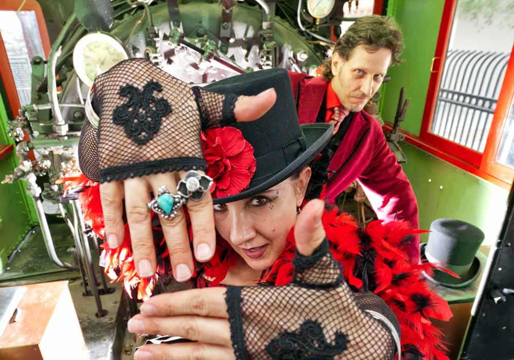 Sarlot and Eyed of Carnival of Illusion posing with costumes in front of a steam locomotive train