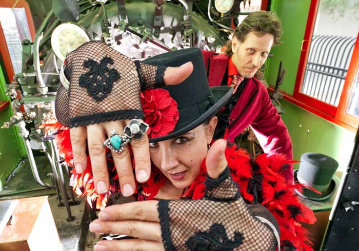 Sarlot and Eyed of Carnival of Illusion posing with costumes in front of a steam locomotive train